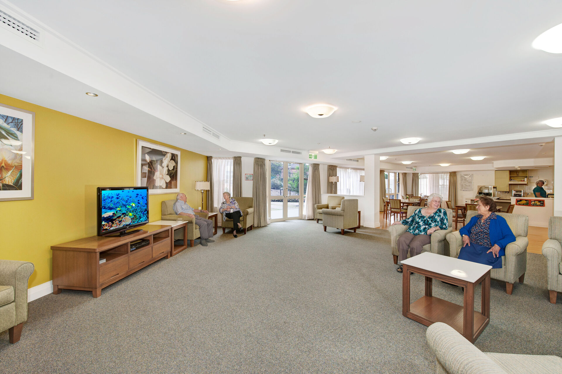 large communal lounge room with aged care residents socialising and watching television at baptistcare warena centre in bangor sutherland shire nsw