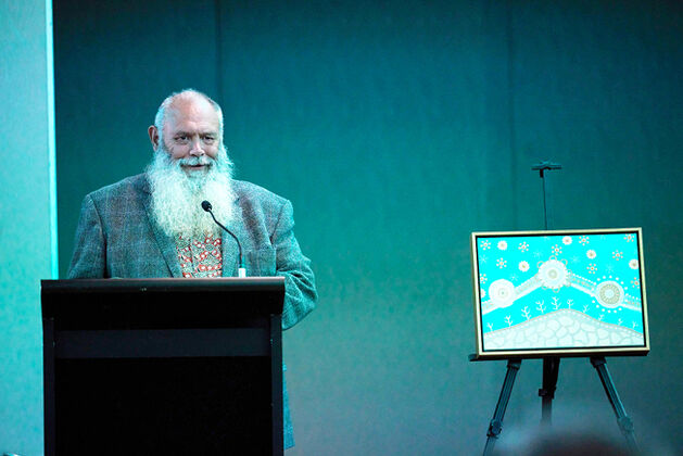 Man at podium speaking next to indigenous artwork
