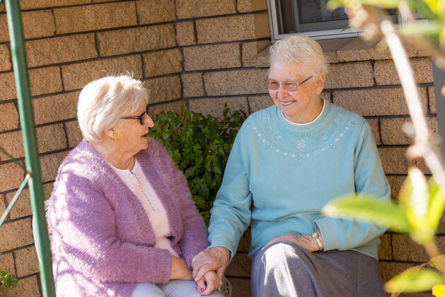 Two elderly women sitting on the outside patio talking and laughing