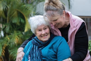 smiling resident of aged care home being embraced outside of the nursing home