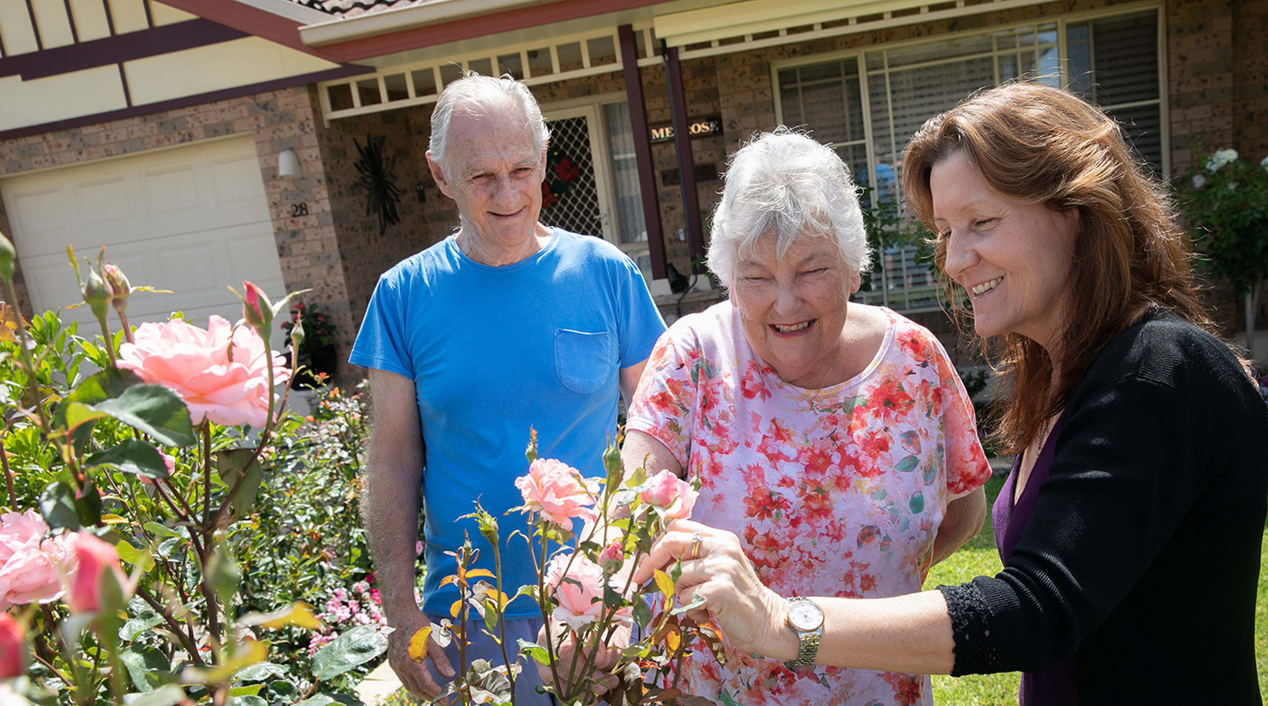 independent over 55s couple enjoying the gardens of their baptistcare retirement village home with baptistcare aged care worker