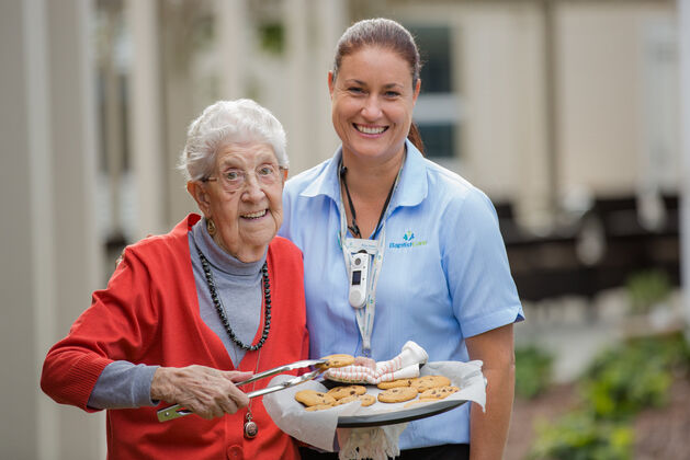 smiling aged care resident serving food with aged care worker in nursing home
