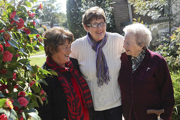 Three elderly women talking outside with arms around each other