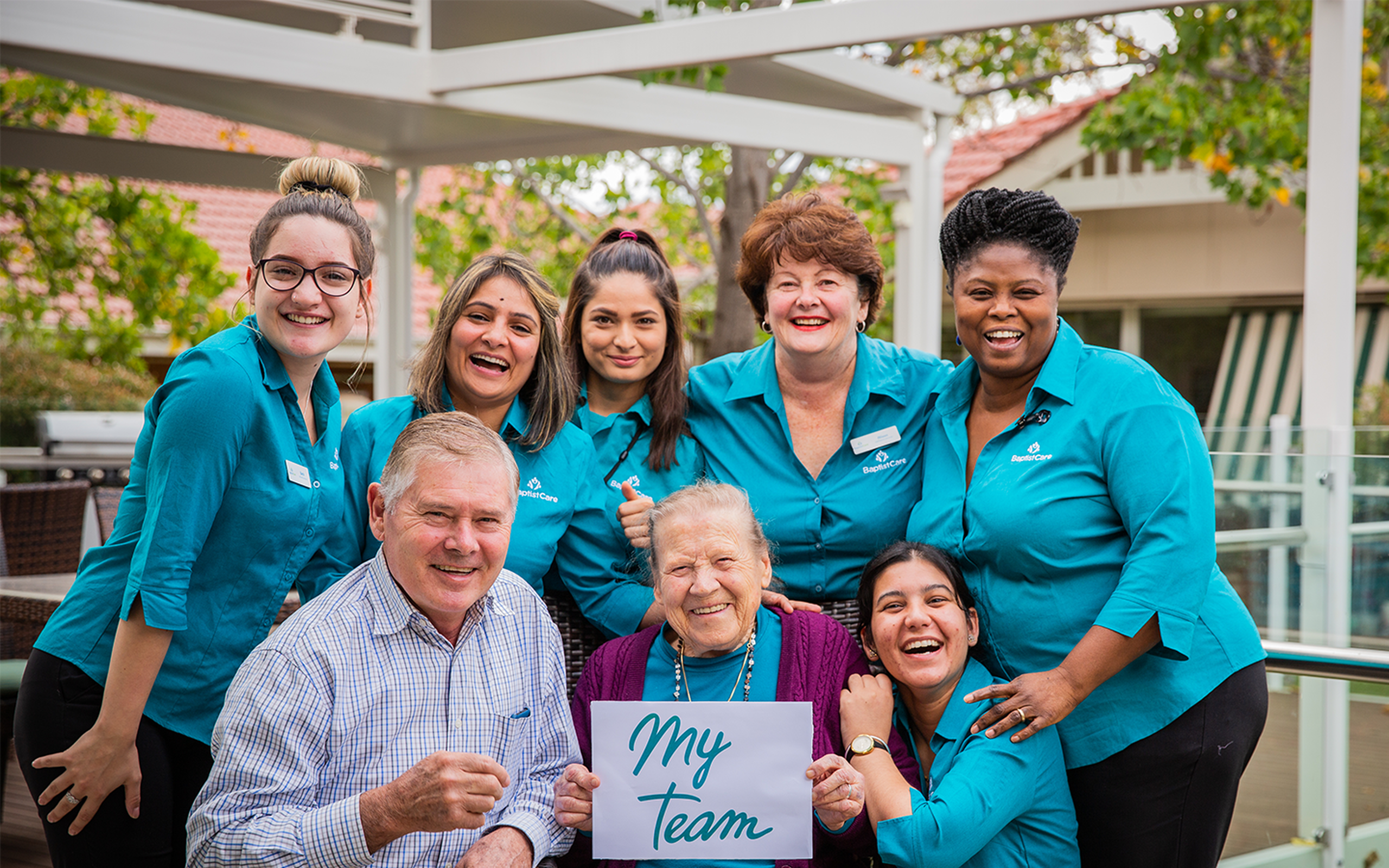 baptistcare aged care workers and chaplain with a nursing home resident with a myteam sign