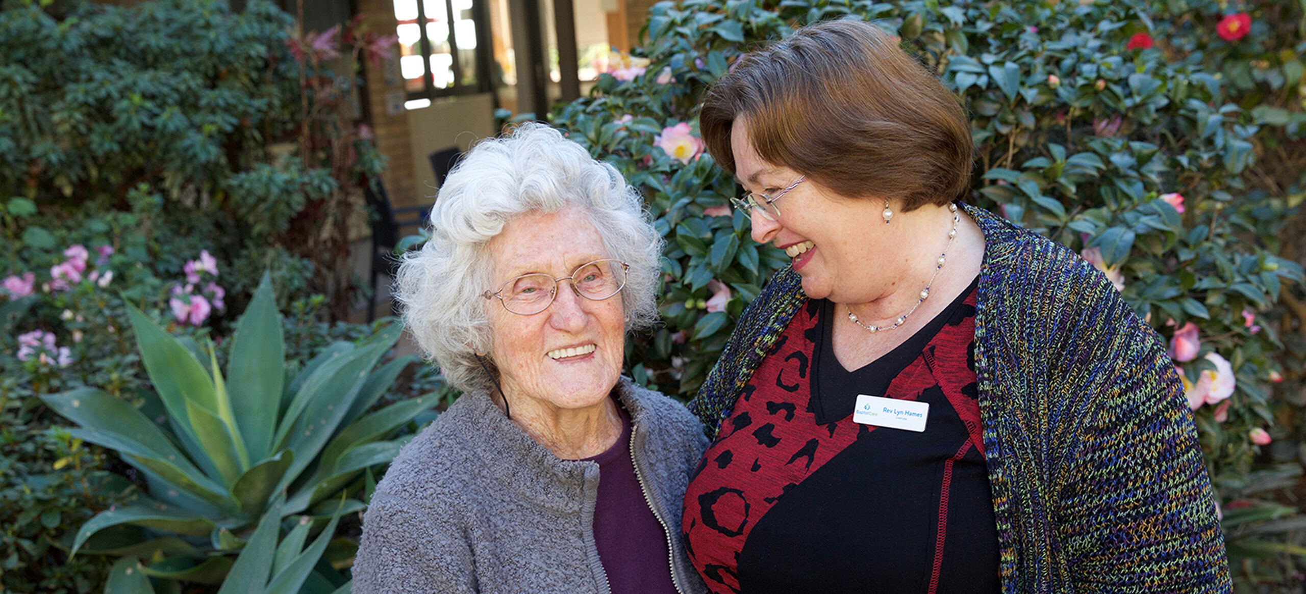 senior aged care resident smiling with a baptistcare aged care chaplain outside of the nursing home
