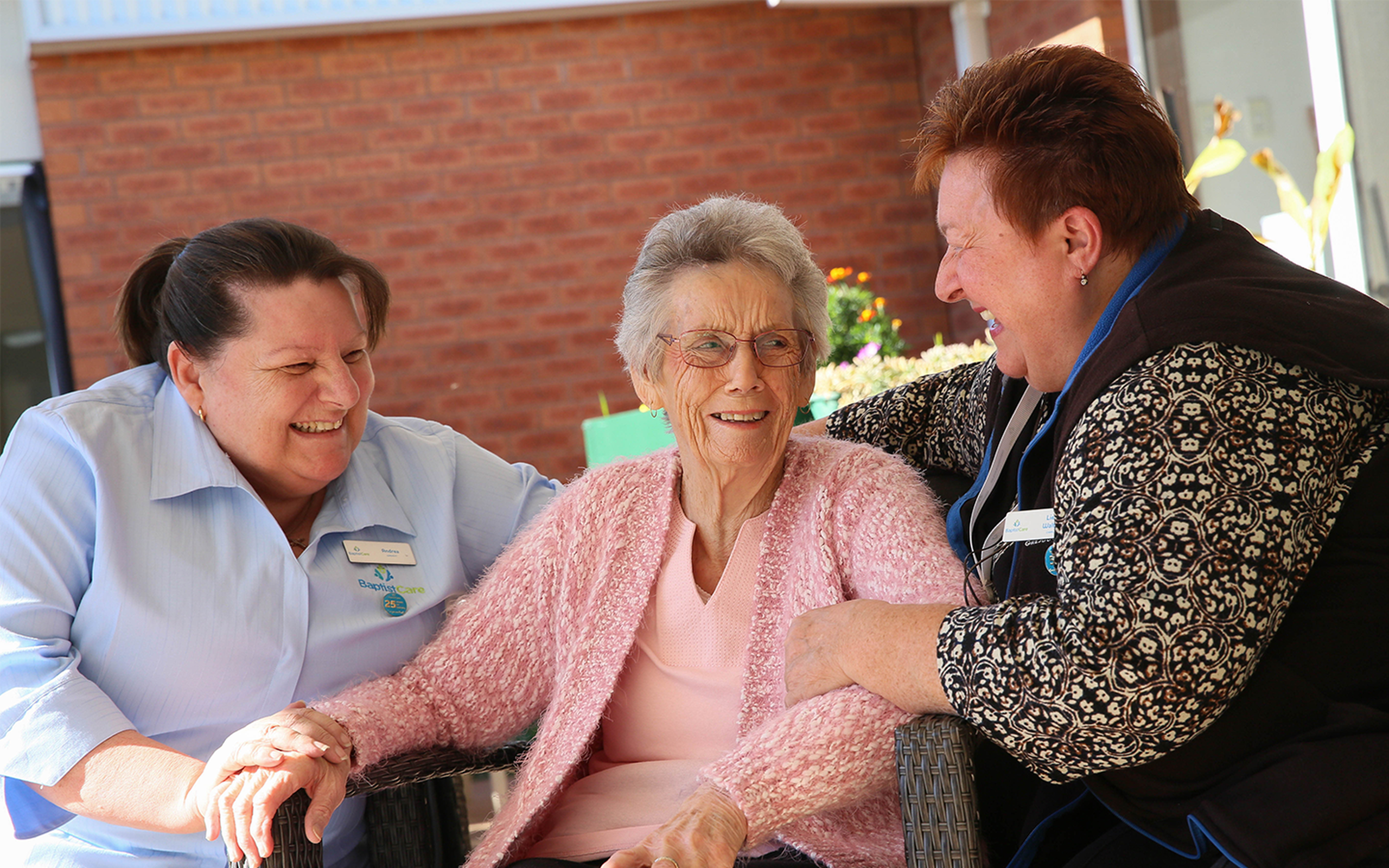 elderly aged care resident sitting down outside the nursing home with two baptistcare aged care workers