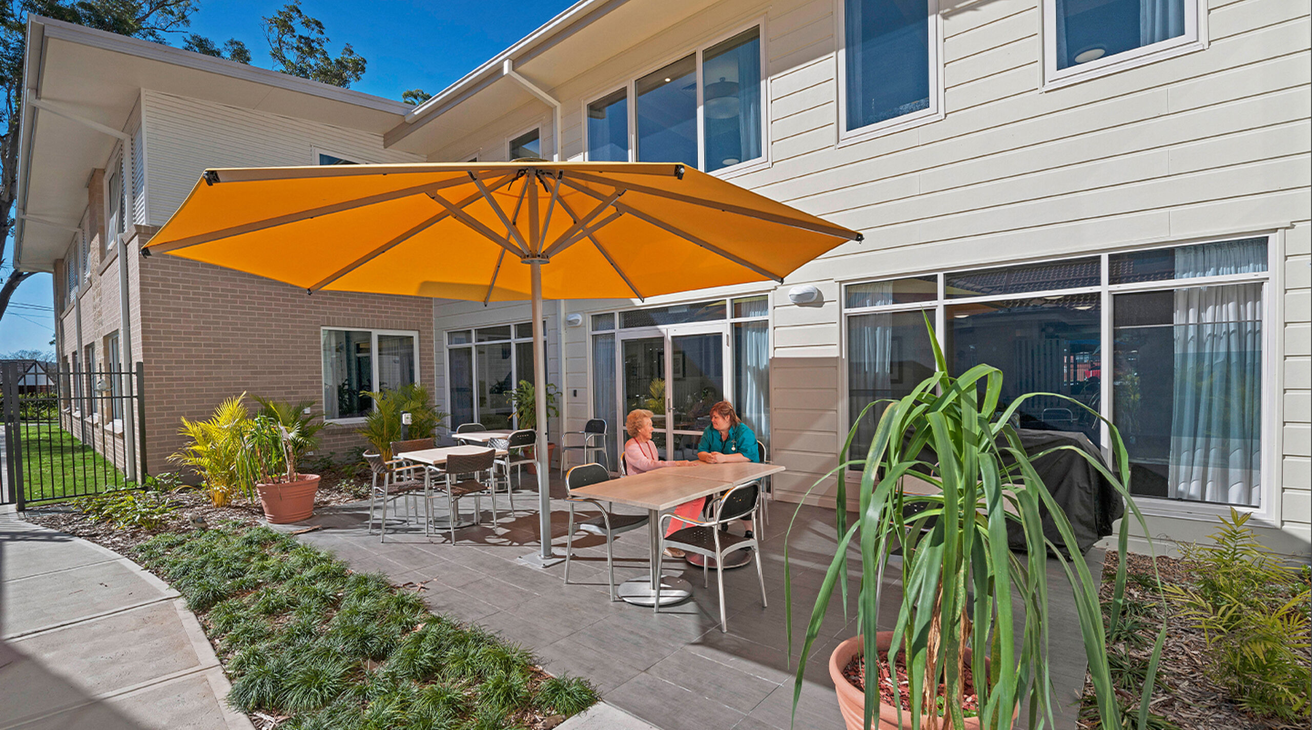 modern two story aged care home with outdoor sitting area covered by a large umbrella overlooking beautiful gardens at baptistcare orana centre aged care home in point clare nsw aged care near gosford central coast