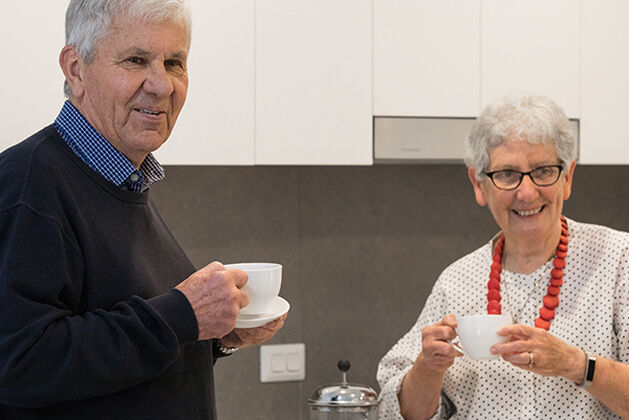 two over 55s enjoying independent living in baptistcare retirement village having tea in the modern kitchen of their retirement community apartment